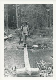 Sara Ashworth walking over a wooden beam crossing a river